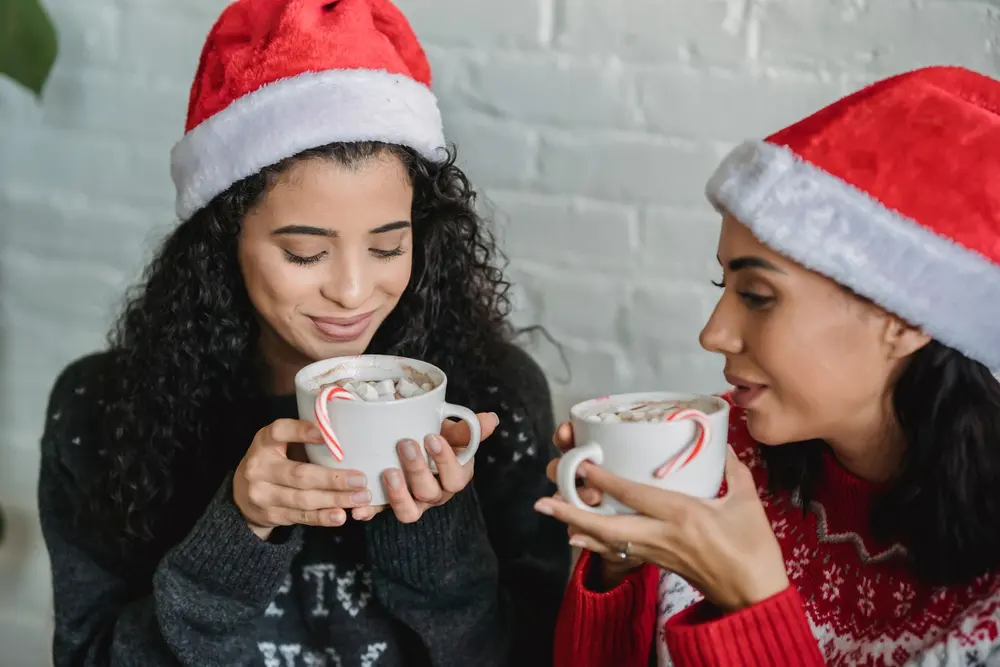 Dos amigas con gorros de Navidad disfrutando una taza de chocolate, tazas personalizadas para navidad en San Cristóbal